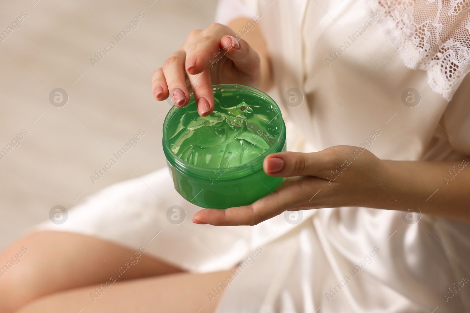 Photo of Young woman holding jar of aloe gel indoors, closeup