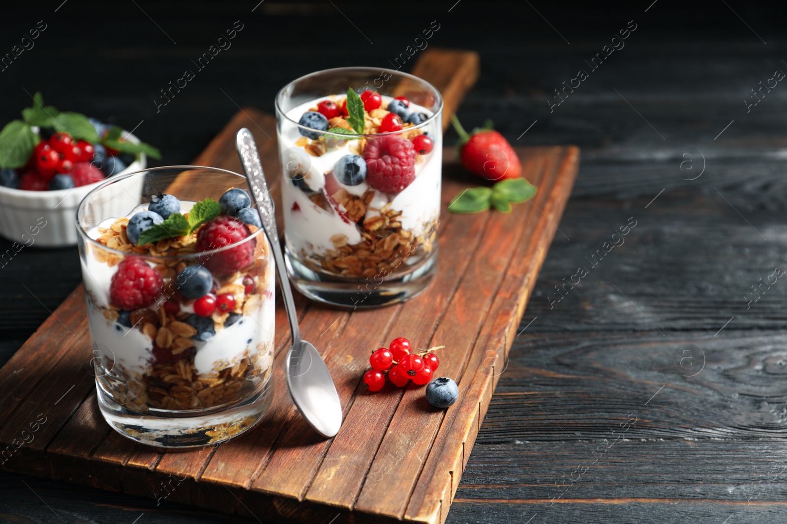 Image of Yummy dessert with granola, yogurt and berries on dark wooden table, space for text