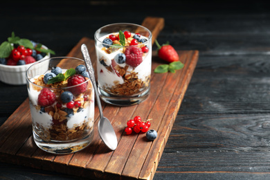 Yummy dessert with granola, yogurt and berries on dark wooden table, space for text