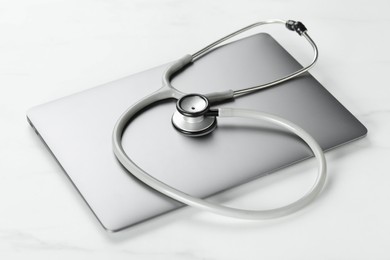 Photo of Modern laptop and stethoscope on white table