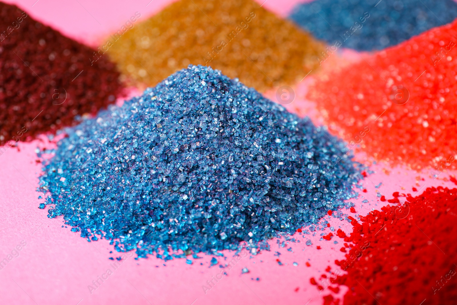 Photo of Heaps of different bright food coloring on pink background, closeup