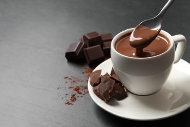 Photo of Spoon with yummy hot chocolate above cup on dark table, space for text