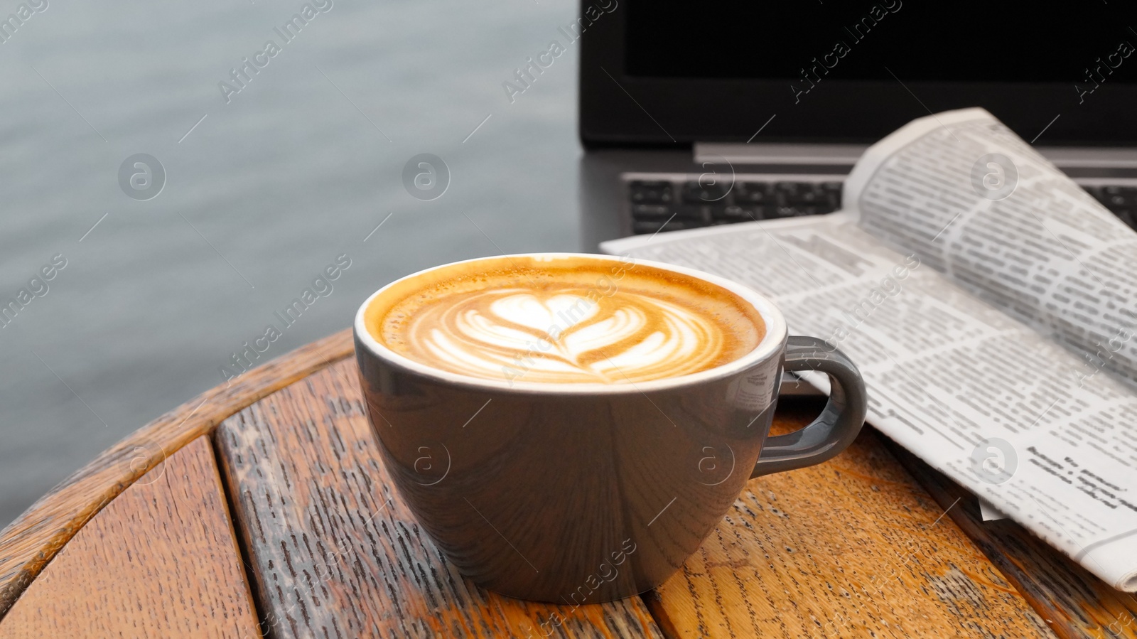 Photo of Cup of delicious coffee, laptop and newspaper on wooden table