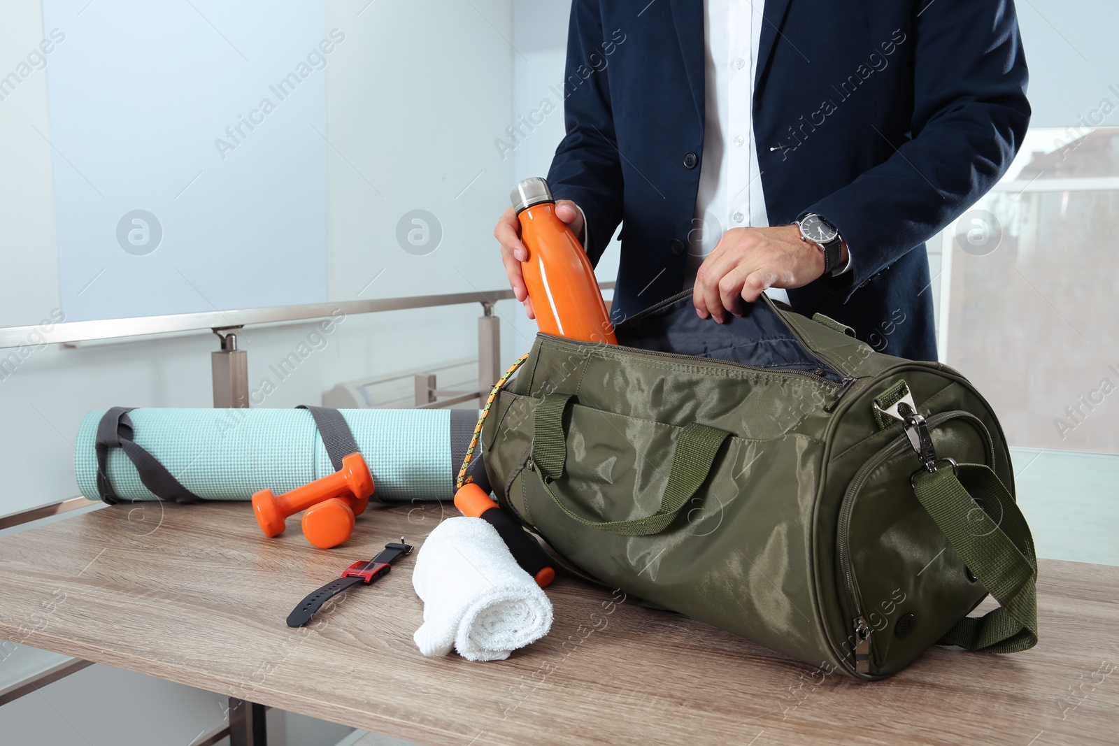 Photo of Businessman packing sports stuff for training into bag in office, closeup