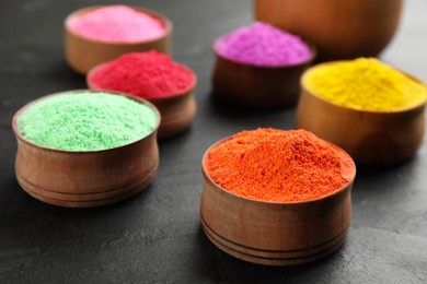 Photo of Colorful powder dyes in bowls on black background, closeup. Holi festival