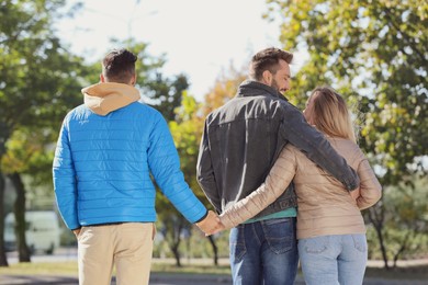 Woman holding hands with another man behind her boyfriend's back during walk in park. Love triangle