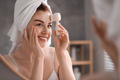 Photo of Washing face. Young woman with cleansing brush near mirror in bathroom