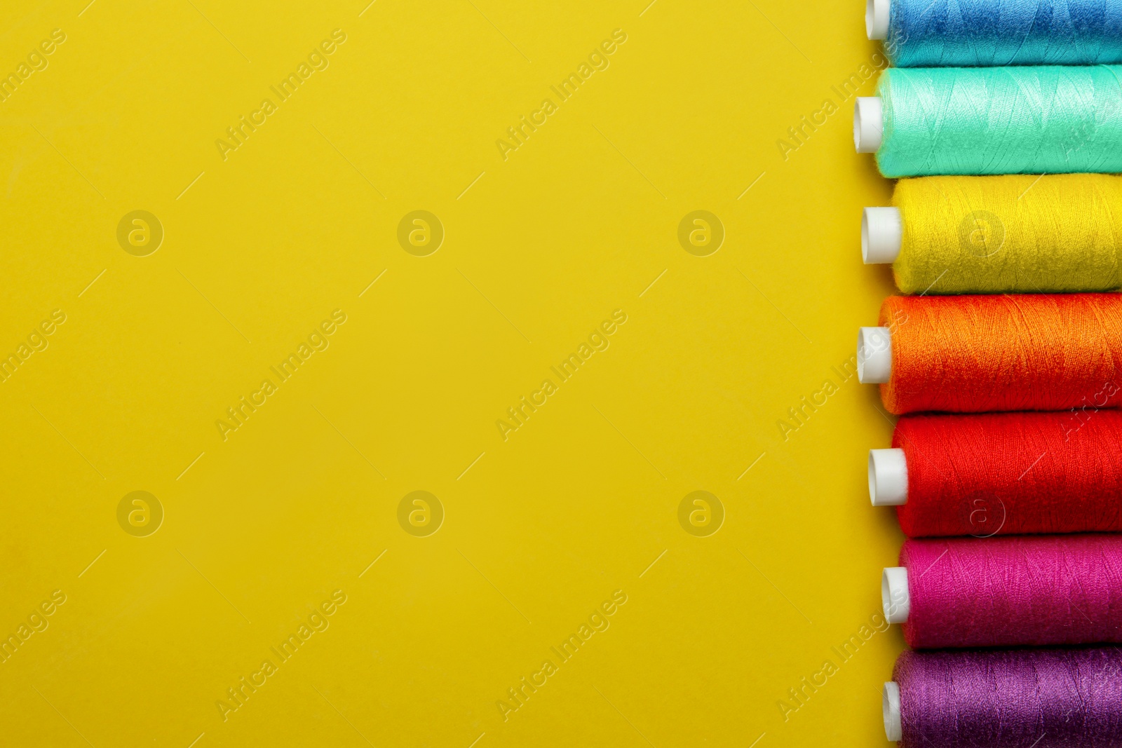 Photo of Set of different colorful sewing threads on yellow background, flat lay. Space for text