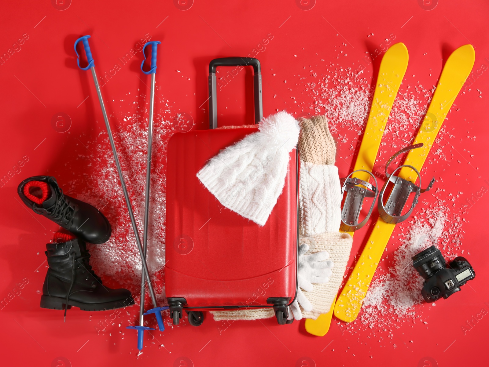 Photo of Suitcase with warm clothes, camera and skis on red background, flat lay. Winter vacation