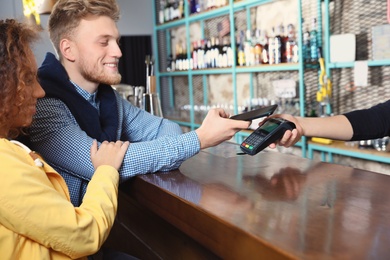 Clients using smartphone and credit card machine for non cash payment in cafe