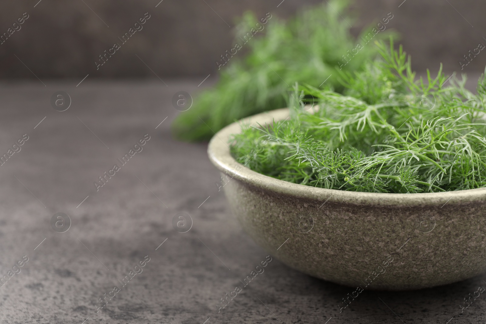Photo of Bowl of fresh dill on grey table, closeup. Space for text