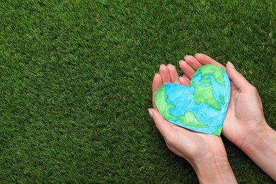 Photo of Happy Earth Day. Woman with heart shaped plasticine planet on green grass, top view and space for text