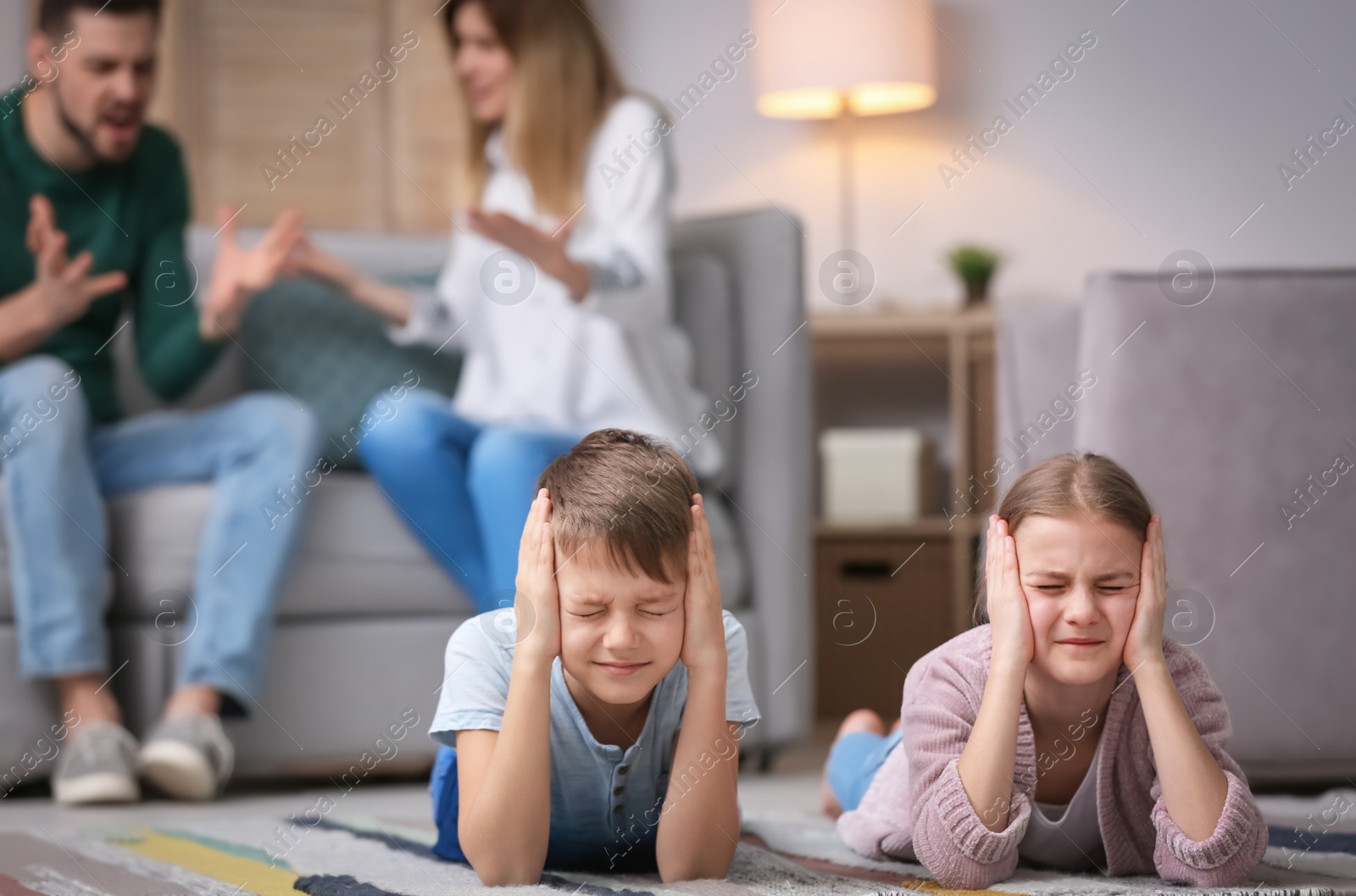 Photo of Little unhappy children lying on floor while parents arguing at home