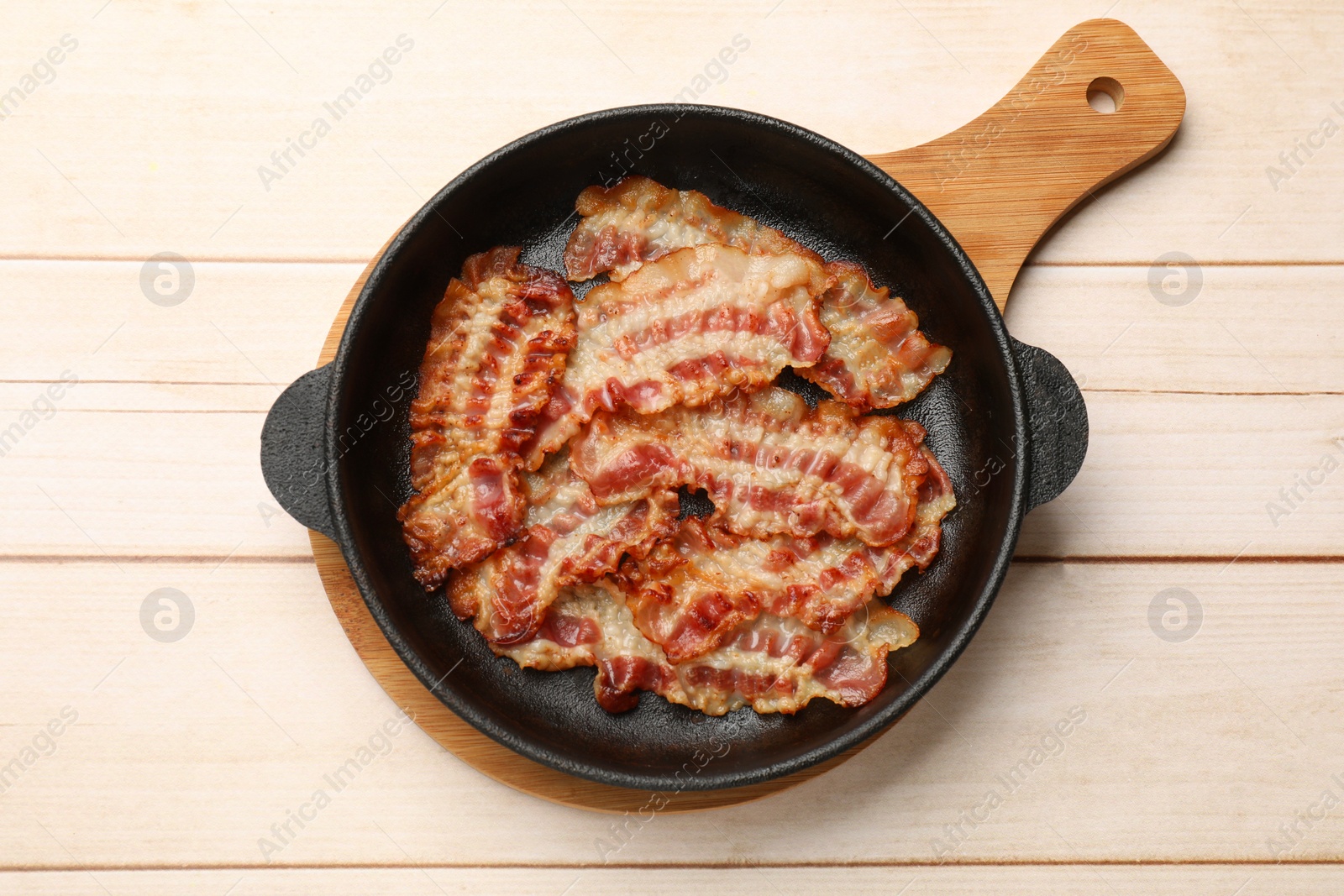Photo of Delicious bacon slices in frying pan on white wooden table, top view