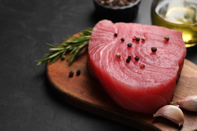 Photo of Raw tuna fillet with spices on black table, closeup. Space for text