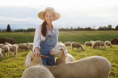 Smiling woman stroking sheep on pasture at farm