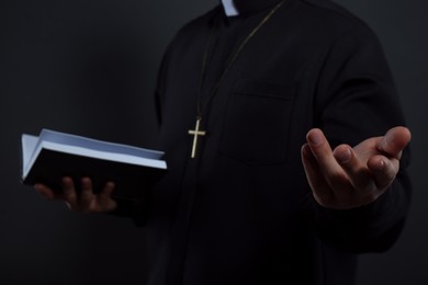 Priest in cassock with Bible on black background, closeup
