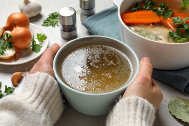 Photo of Woman with cup of hot delicious bouillon at light grey table, closeup