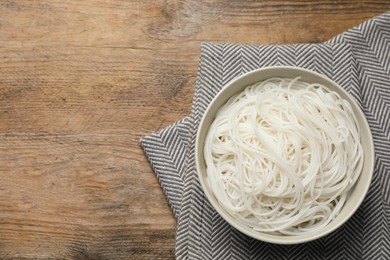 Photo of Bowl with cooked rice noodles on wooden table, top view. Space for text