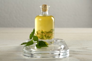 Photo of Glass bottle of nettle oil and leaves on white wooden table