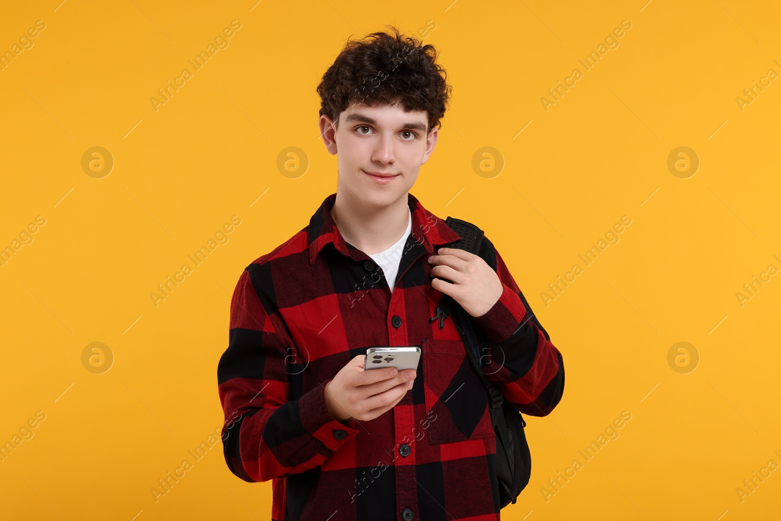 Photo of Portrait of student with backpack and smartphone on orange background