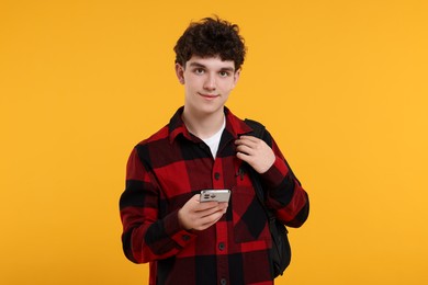 Photo of Portrait of student with backpack and smartphone on orange background