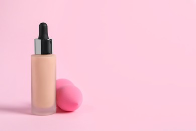 Photo of Bottle of skin foundation and sponge on pink background, space for text. Makeup product