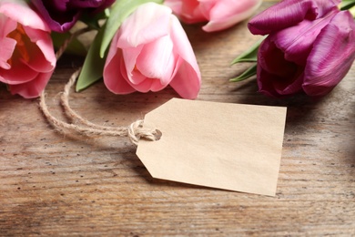 Beautiful spring tulips and blank label on wooden background, space for text. International Women's Day