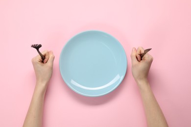 Photo of Woman with fork, knife and empty plate at pink table, top view