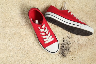 Red sneakers and mud on beige carpet, top view