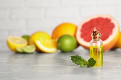 Photo of Bottle of essential oil with different citrus fruits and mint on grey marble table. Space for text