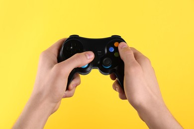 Man using wireless game controller on yellow background, closeup