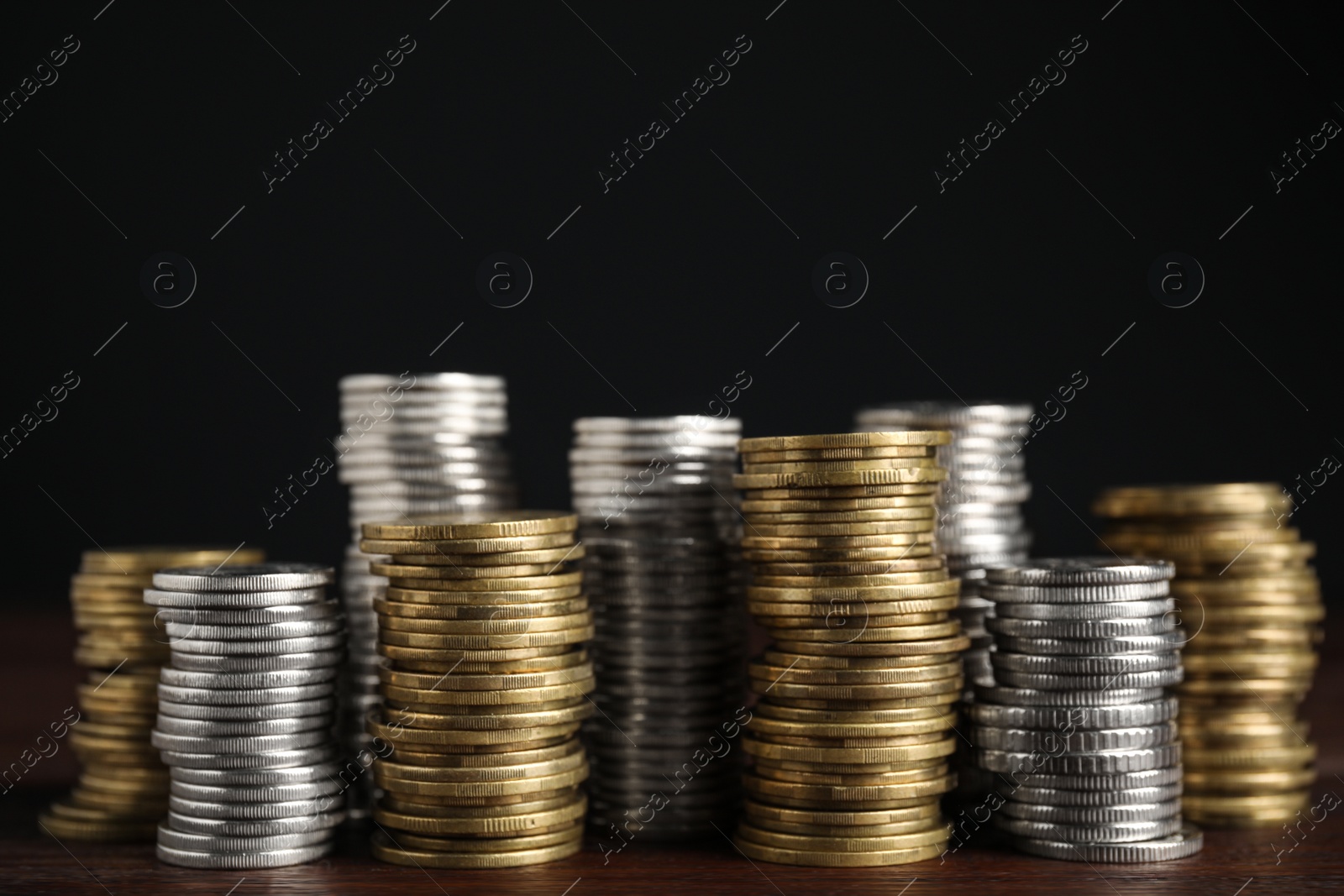 Photo of Many coins stacked on wooden table against black background