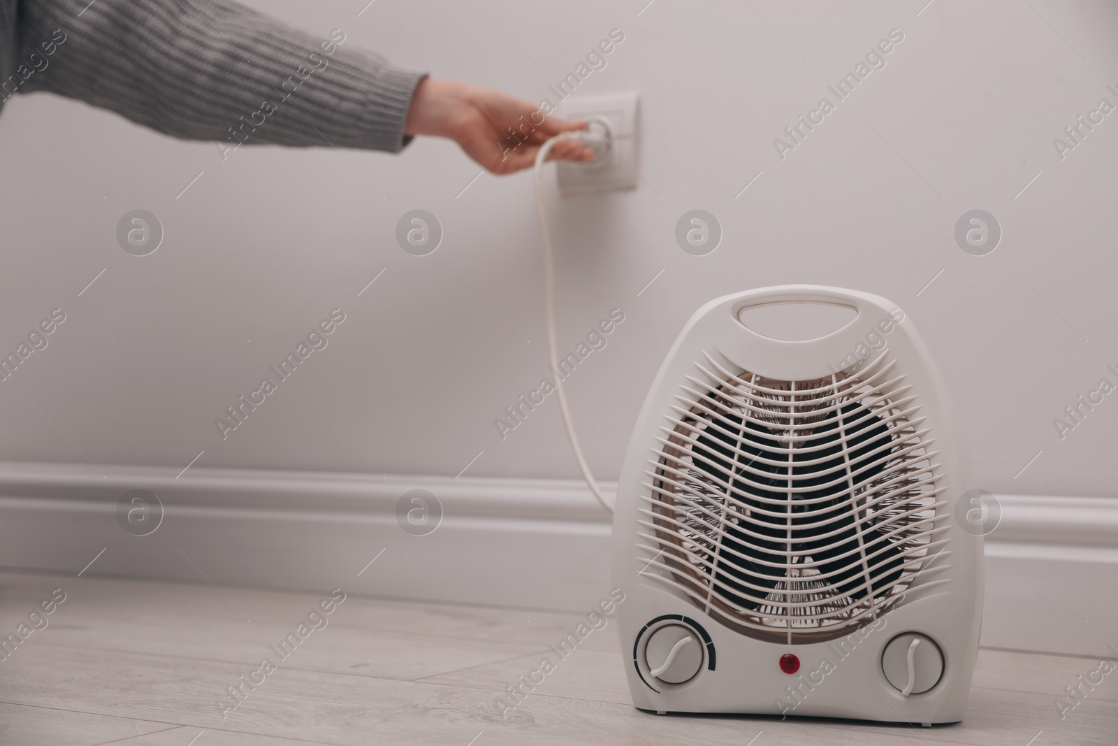 Photo of Woman plug in modern electric fan heater indoors, focus on device. Space for text