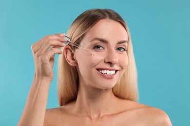 Beautiful woman applying cosmetic serum onto her face on light blue background