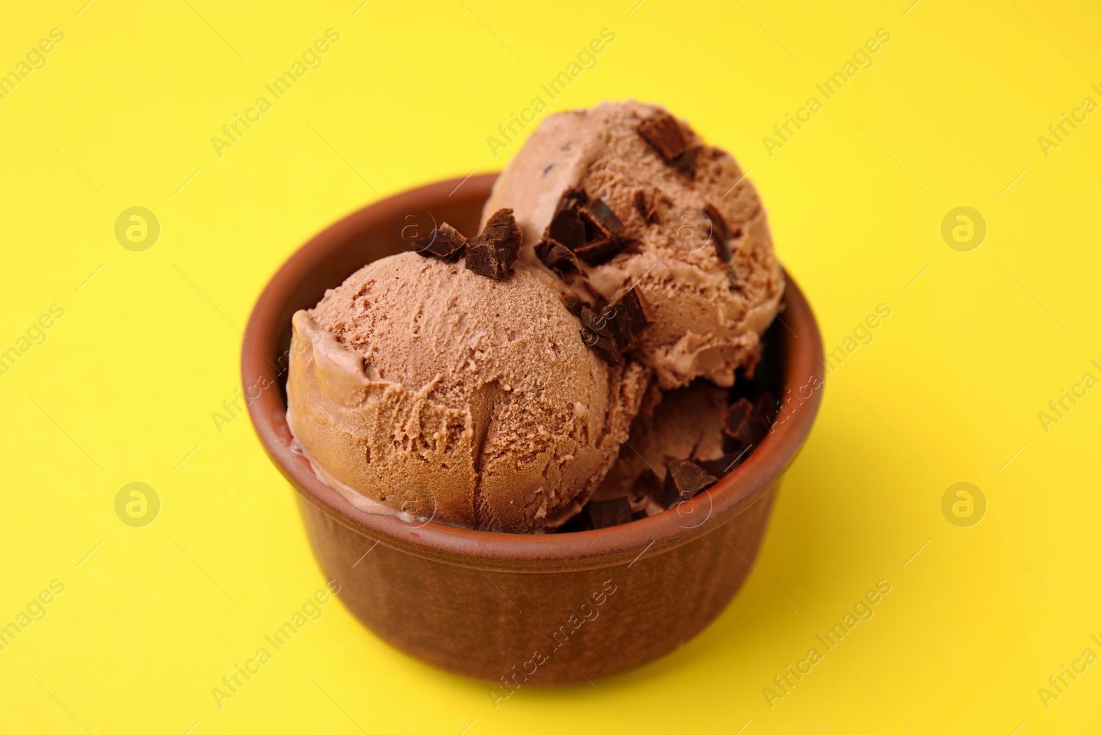 Photo of Bowl of tasty ice cream with chocolate chunks on yellow background, closeup