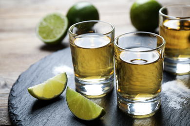 Photo of Mexican Tequila shots, lime slices and salt on wooden table