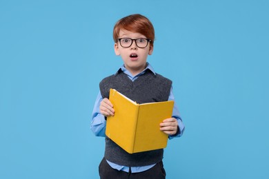 Photo of Cute schoolboy with book on light blue background