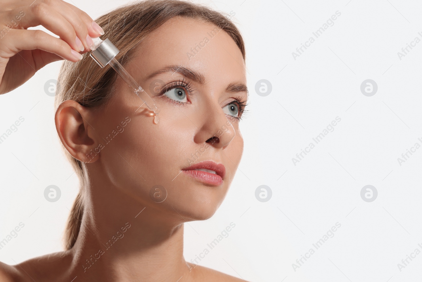 Photo of Beautiful woman applying cosmetic serum onto her face on white background, space for text