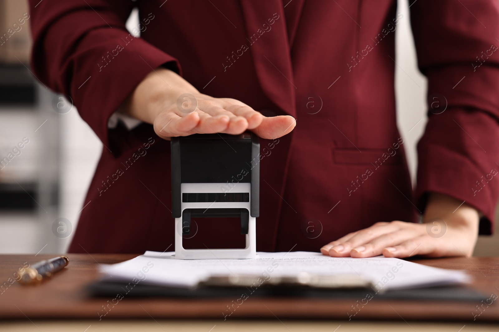 Photo of Notary stamping document at table in office, closeup