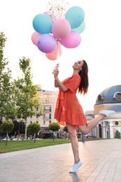 Cheerful young woman with color balloons outdoors on sunny day