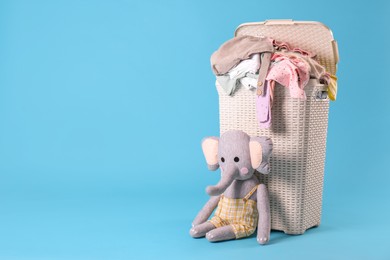 Photo of Laundry basket with baby clothes and soft toy on light blue background. Space for text