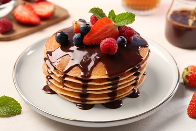 Stack of tasty pancakes with fresh berries, chocolate sauce and mint on white table, closeup