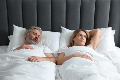 Photo of Irritated woman lying near her snoring husband in bed at home
