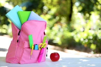 Backpack with school stationery on table outdoors