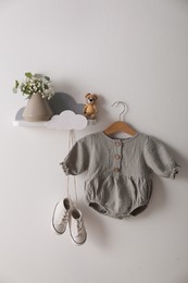 Photo of Cute baby onesie and shoes hanging on white wall
