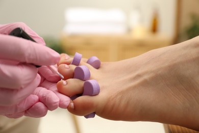 Professional pedicurist painting client`s toenails with polish in beauty salon, closeup