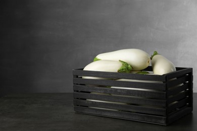 Wooden crate with white eggplants on black textured table against grey background. Space for text