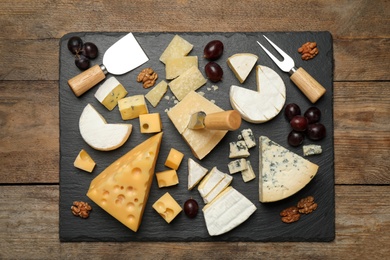 Photo of Cheese platter with specialized knives and fork on wooden table, top view