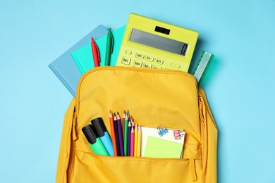 Backpack with different school stationery on light blue background, top view
